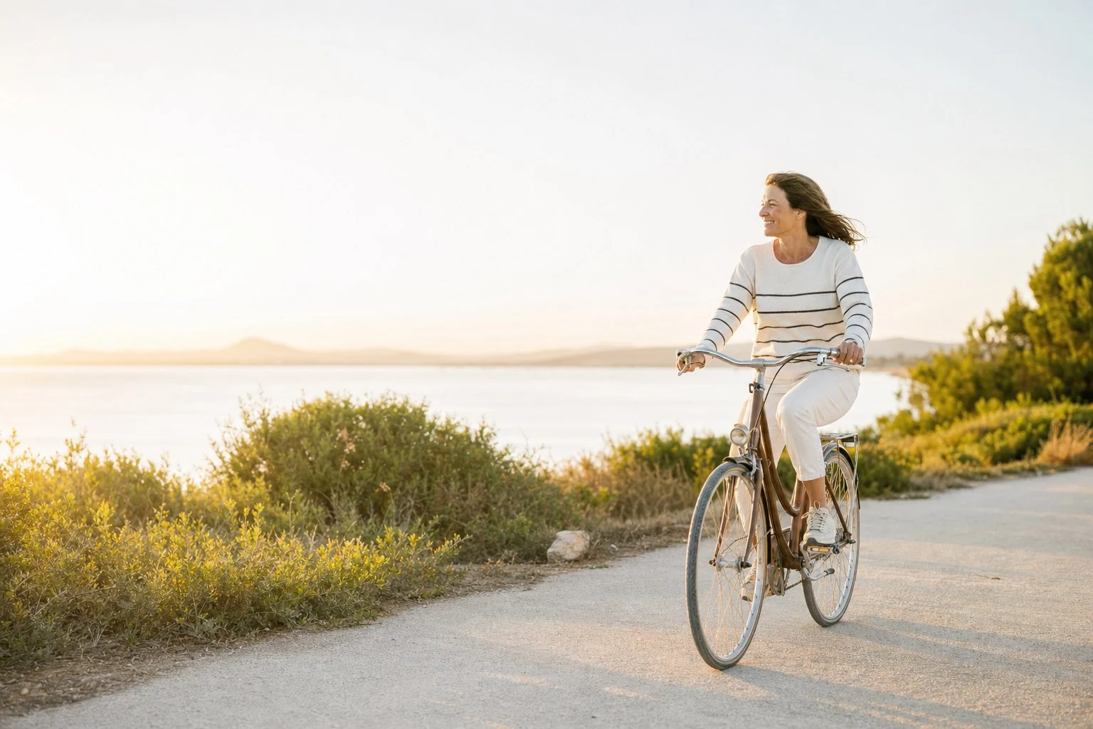 Mujer montando en bicicleta por un camino cercano al mar.